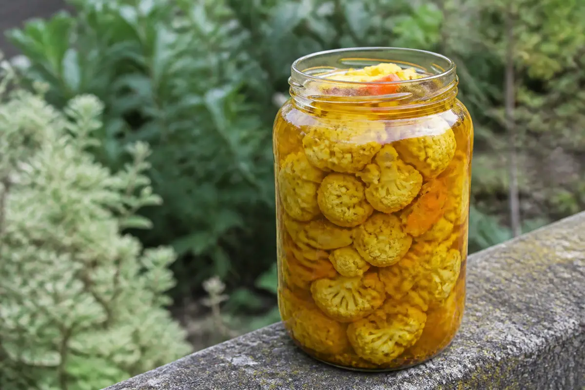 Bocal de pickles de chou-fleur sur muret en pierre avec fond végétal flou
